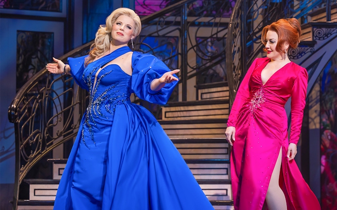 Two performers in elegant dresses on stage during "Death Becomes Her" show.