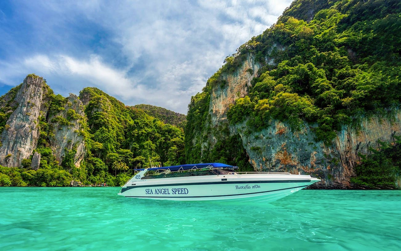 Speedboat cruising in Pileh Bay with limestone cliffs and turquoise water.