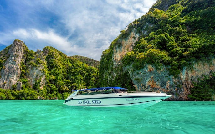 Speedboat cruising in Pileh Bay with limestone cliffs and turquoise water.