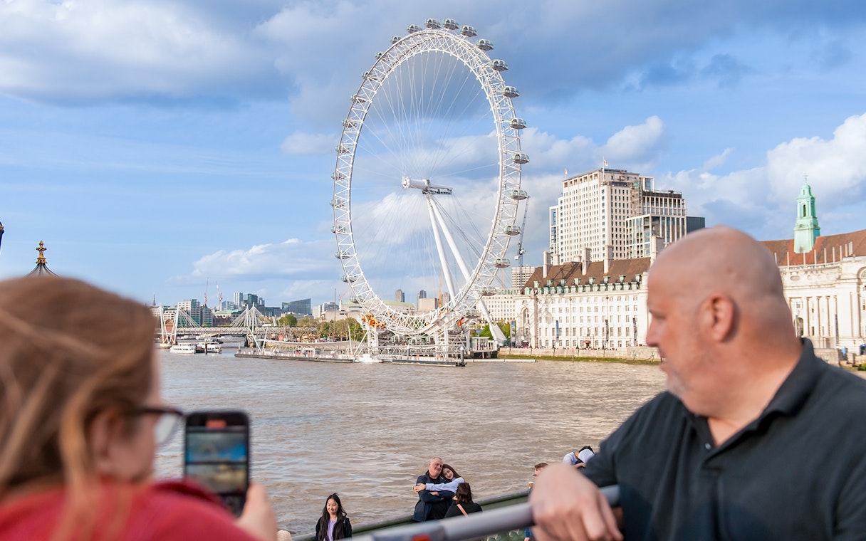 Couple taking photos with the London Eye in the background.