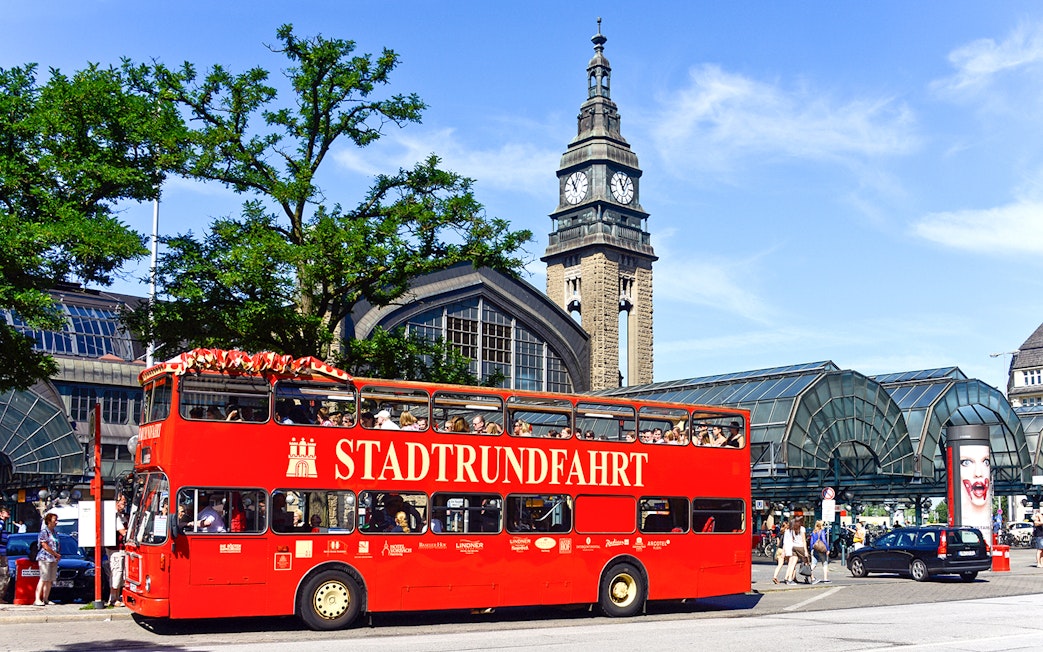 Stadtrundfahrt bus in front of Hamburg Central Station with clock tower.