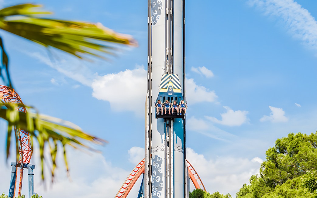 Riders on The Shuttle drop tower at Parque de Atracciones de Madrid against blue sky.