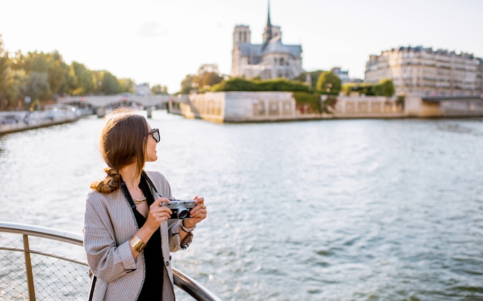 Person holding a camera on a Seine River cruise with Notre-Dame Cathedral in the background.
