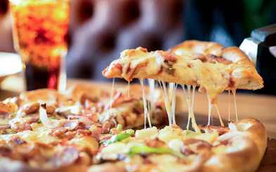 Cheese pizza slice being lifted with a drink in the background.