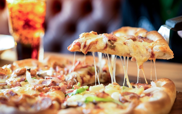 Cheese pizza slice being lifted with a drink in the background.
