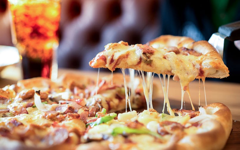 Cheese pizza slice being lifted with a drink in the background.
