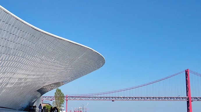 MAAT museum exterior with visitors and Lisbon's 25 de Abril Bridge in the background.