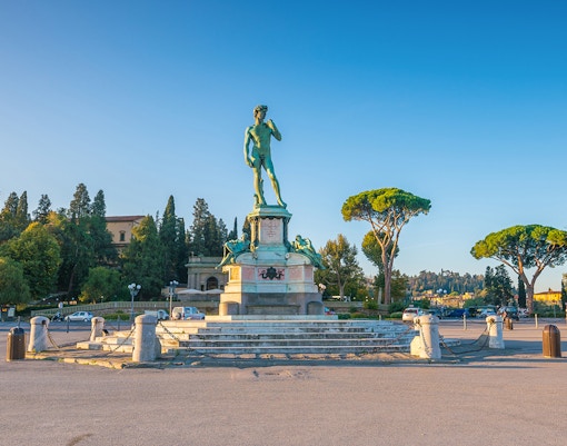 Statue of David replica at Piazzale Michelangelo, Florence, with surrounding trees and clear sky.