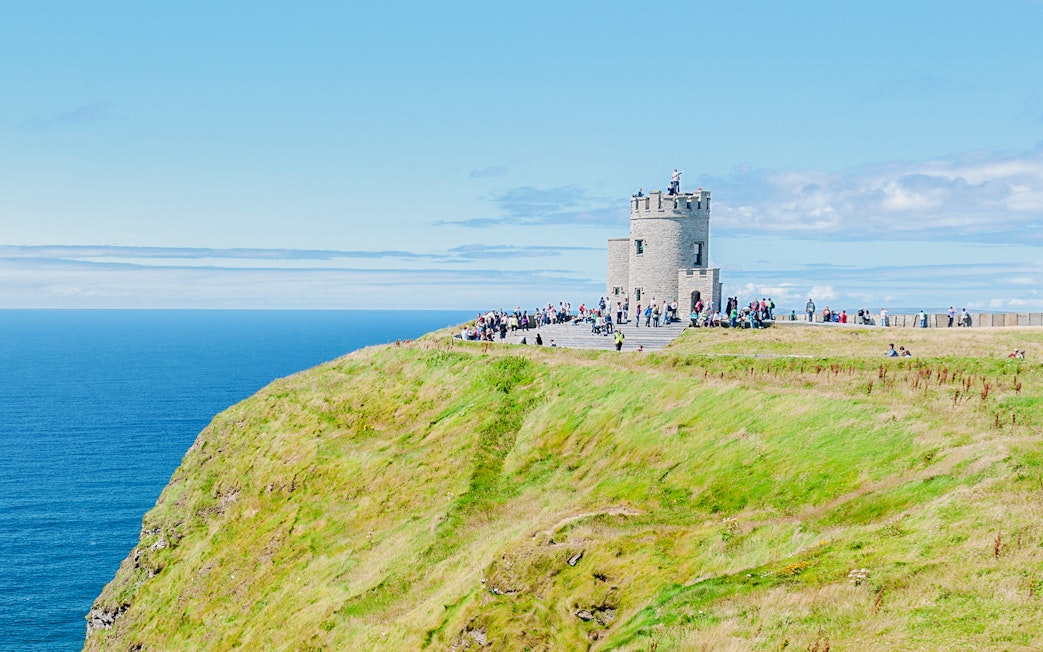 O'Brien's Tower on the Cliffs of Moher with visitors overlooking the Atlantic Ocean.