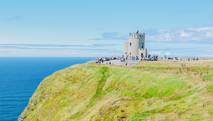 O'Brien's Tower on the Cliffs of Moher with visitors overlooking the Atlantic Ocean.