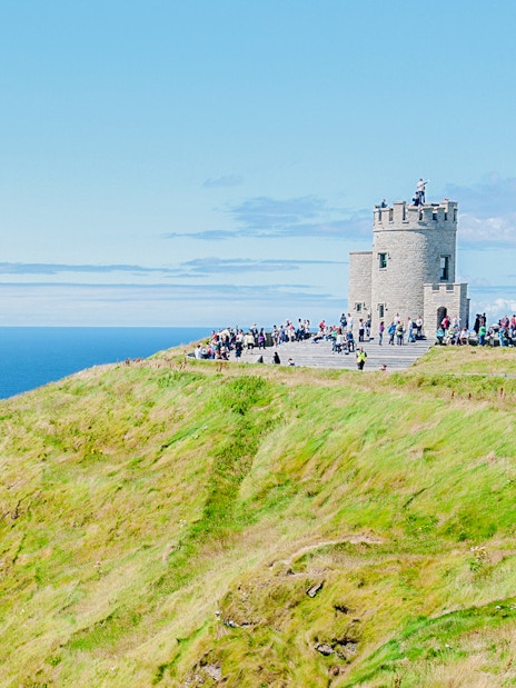 O'Brien's Tower on the Cliffs of Moher with visitors overlooking the Atlantic Ocean.