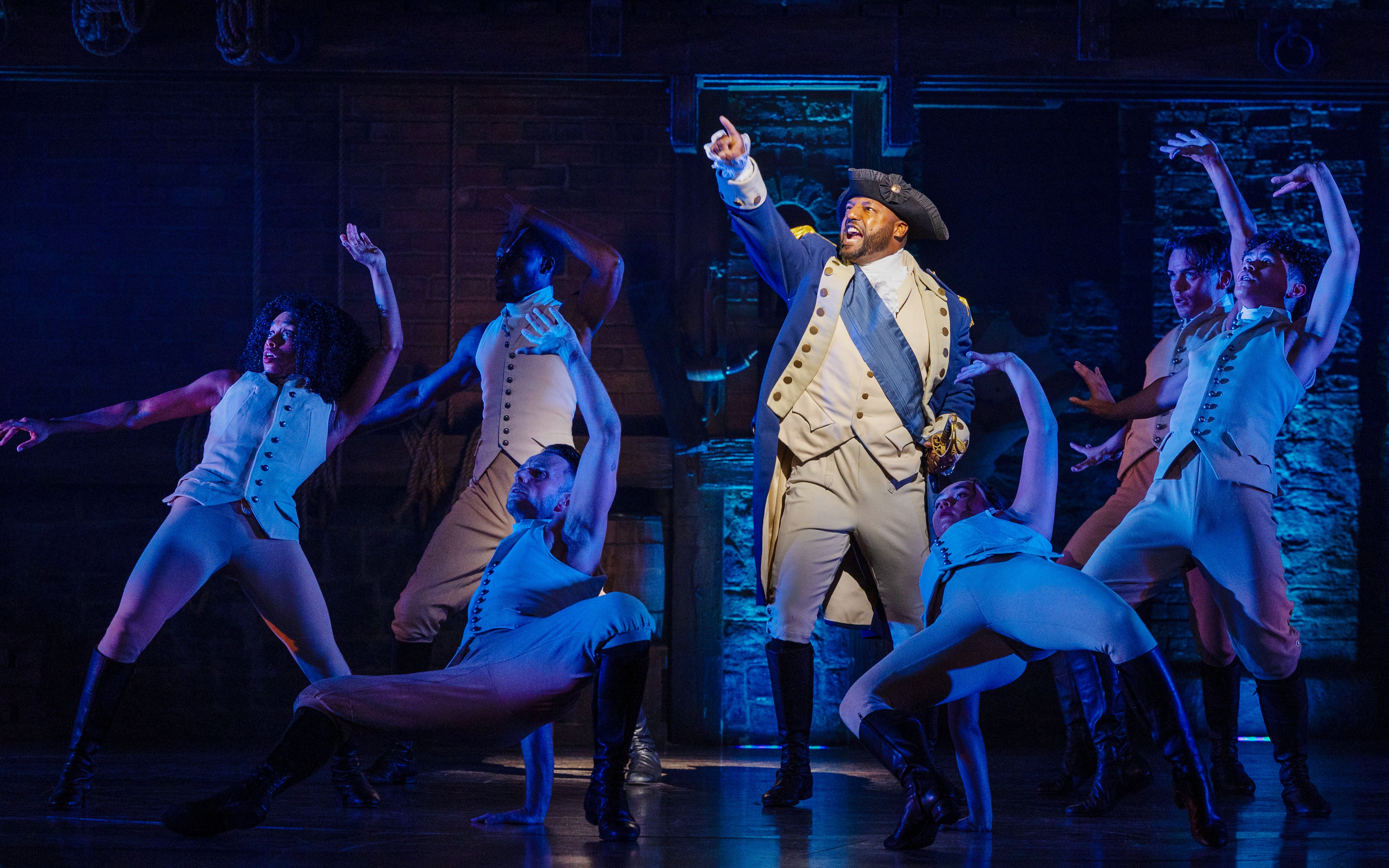 Cast performing a scene from the Hamilton musical on stage.