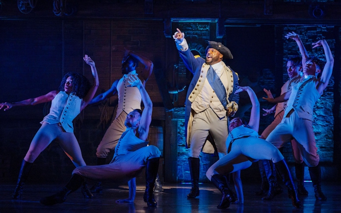 Cast performing a scene from the Hamilton musical on stage.