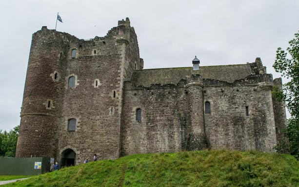 Doune Castle in Scotland with stone walls and a flag on the tower.