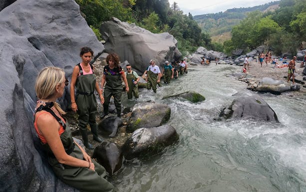 Group trekking through Gole Alcantara river with rocky landscape in Sicily.