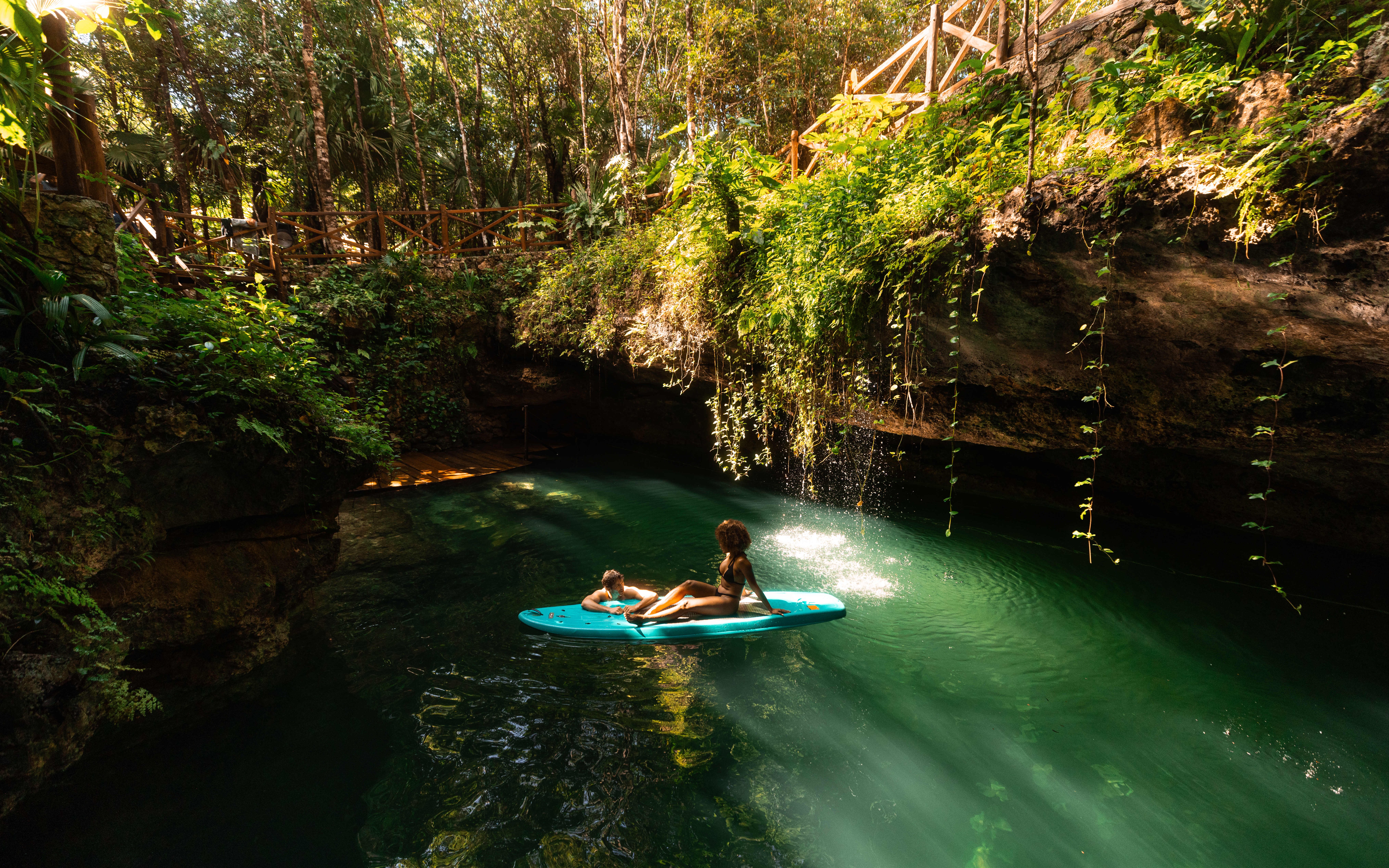 Couple relaxing on a paddleboard in a lush cenote surrounded by greenery.