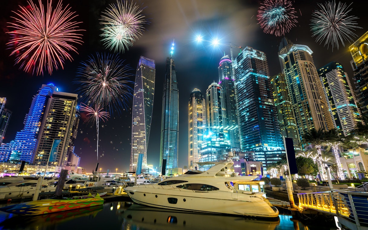 Fireworks over Dubai Marina with yachts and skyscrapers illuminated at night, UAE.