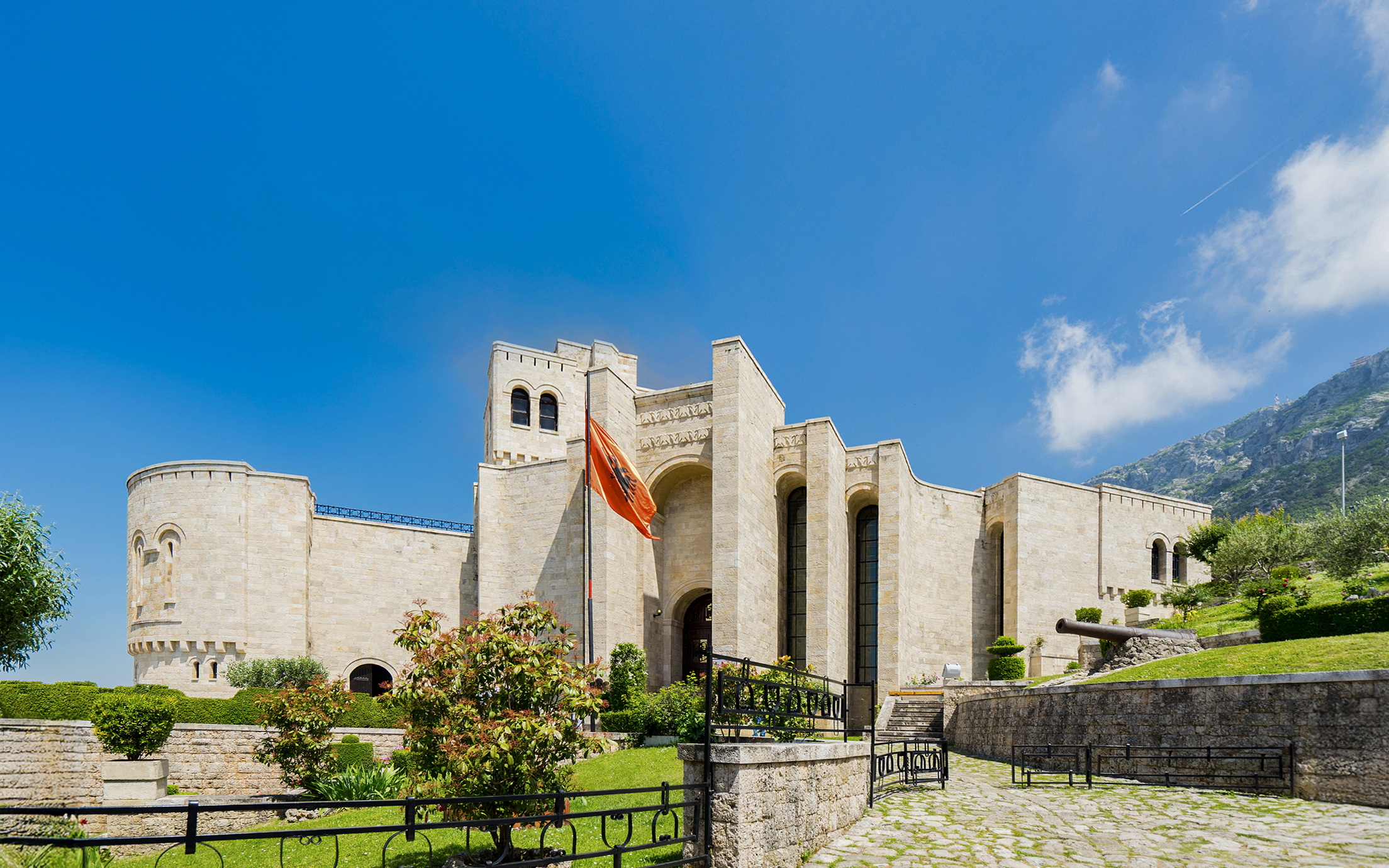 Krujë Castle with Albanian flag, set against a mountainous backdrop in Krujë, Albania.