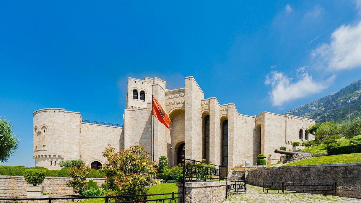 Krujë Castle with Albanian flag, set against a mountainous backdrop in Krujë, Albania.