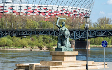 Mermaid statue on Vistula River with Warsaw's National Stadium in the background.