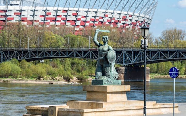 Mermaid statue on Vistula River with Warsaw's National Stadium in the background.