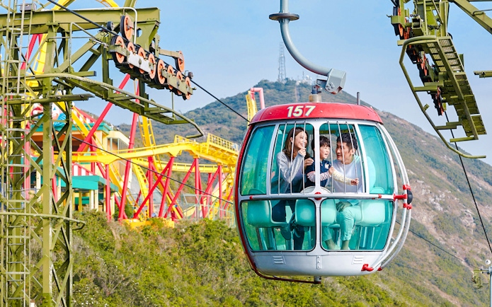 Family enjoying a cable car ride at Ocean Park Hong Kong with colorful rides in the background.