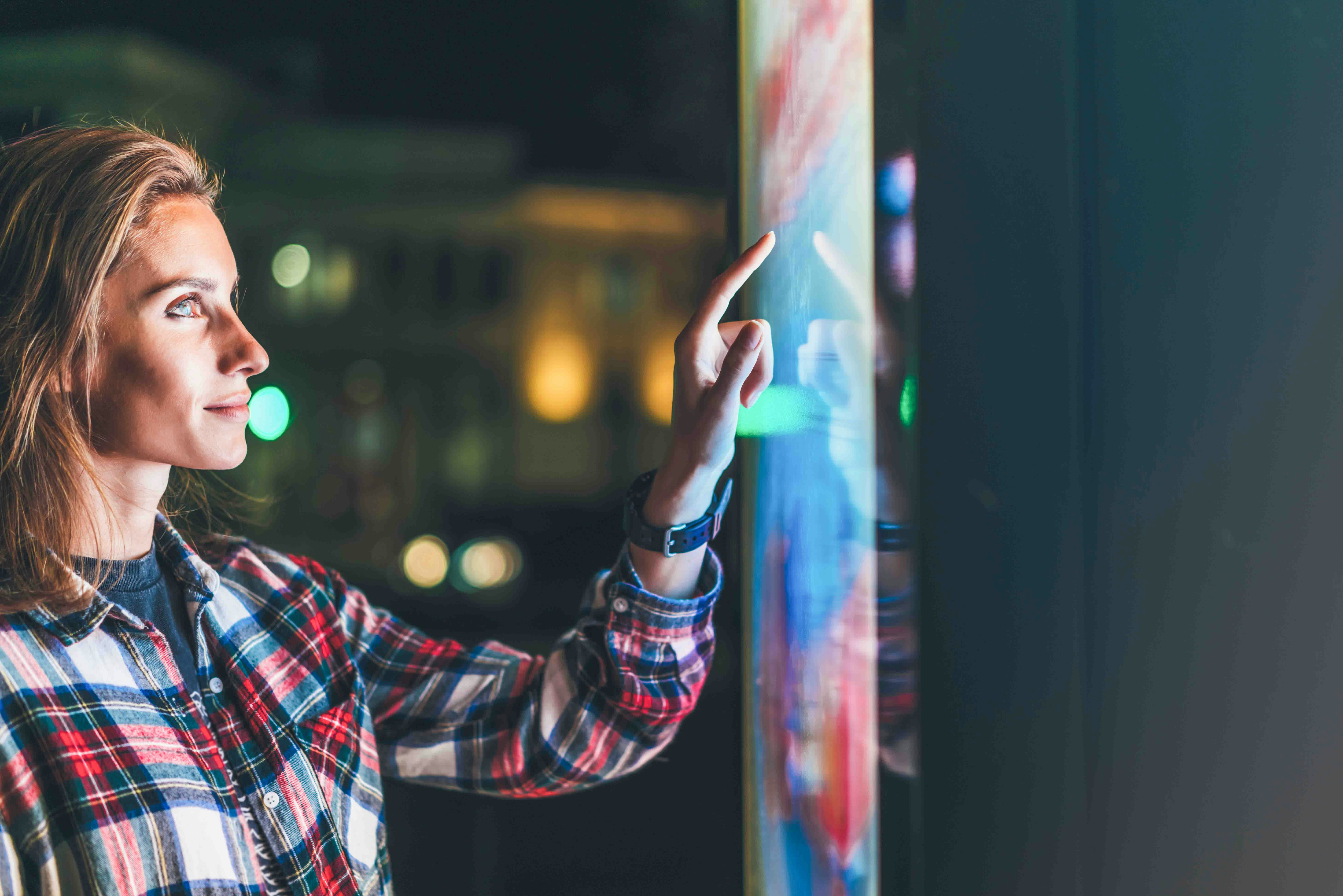 Person interacting with a touch screen at night, city lights in the background.