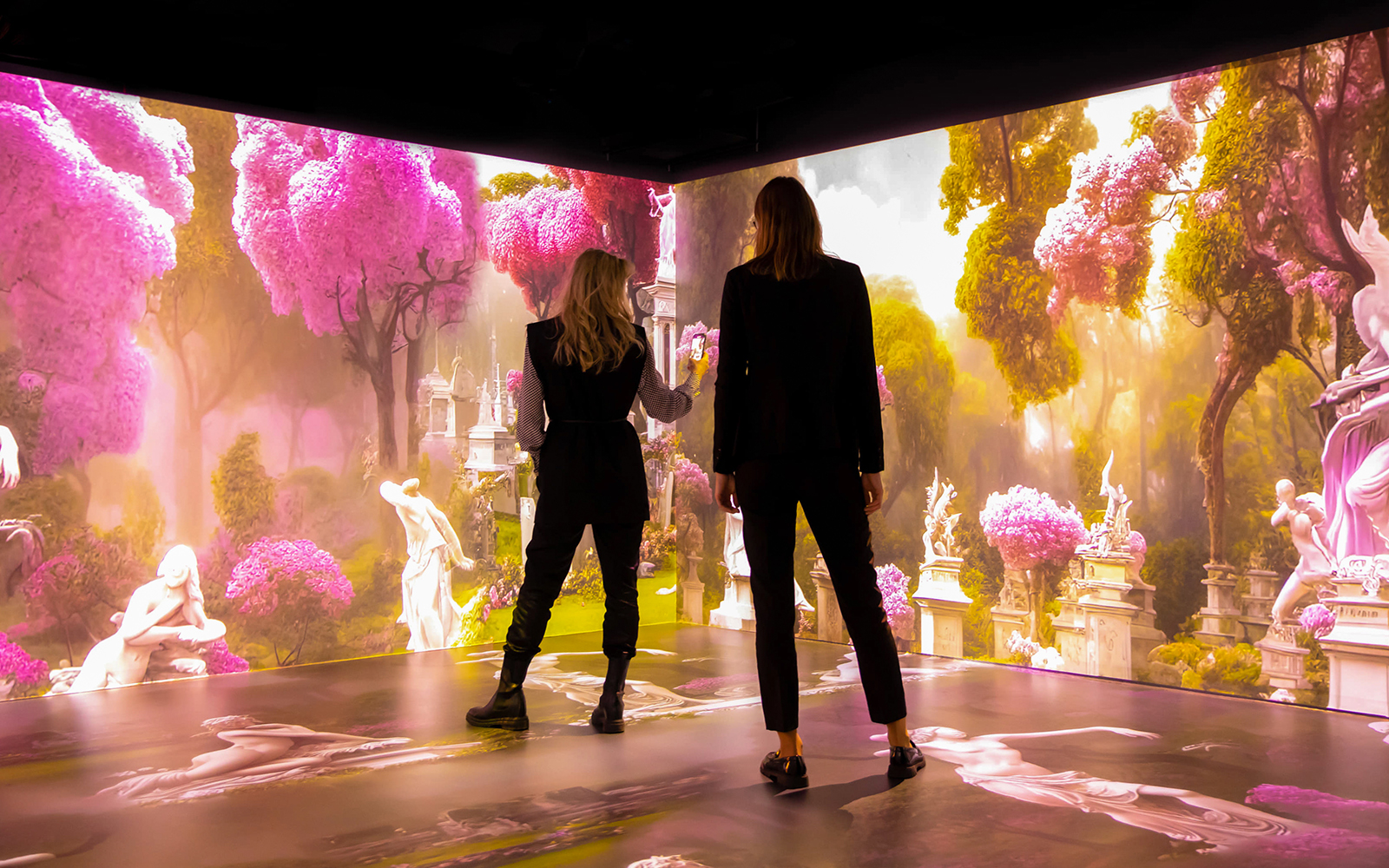 Visitors exploring immersive Mythos Mozart exhibit with vibrant pink trees and classical statues.