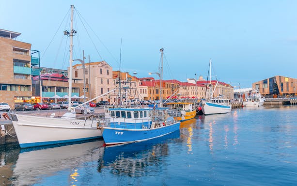 Boats docked at a waterfront in Hobart, Tasmania, with historic buildings in the background.