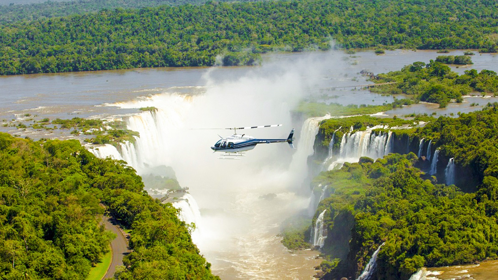 Helicopter flying over Iguazú Falls surrounded by lush greenery.