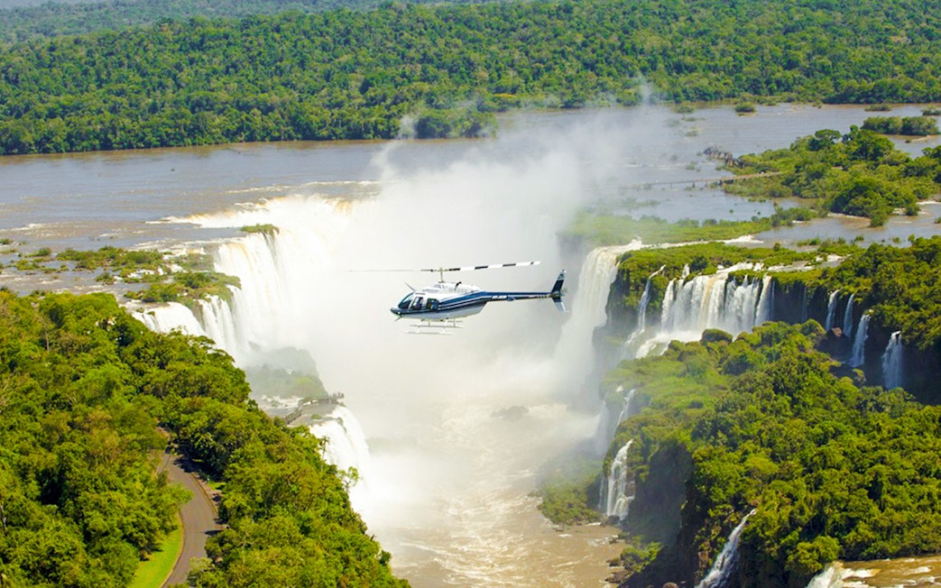 Helicopter flying over Iguazú Falls surrounded by lush greenery.
