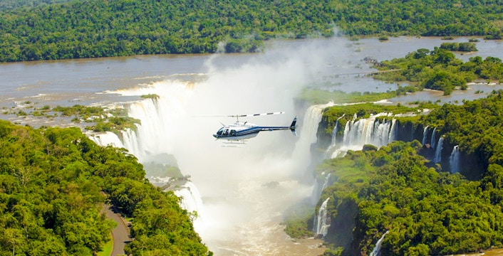 Helicopter flying over Iguazú Falls surrounded by lush greenery.