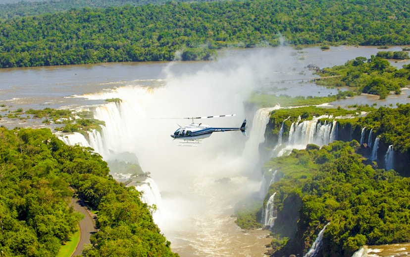 Helicopter flying over Iguazú Falls surrounded by lush greenery.