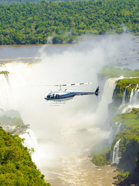 Helicopter flying over Iguazú Falls surrounded by lush greenery.