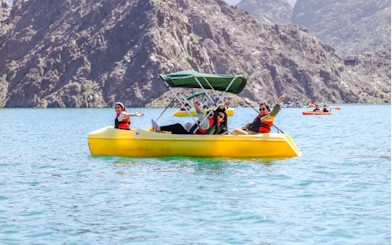 People enjoying a pedal boat ride on Hatta Lake with mountain views, Sharjah.