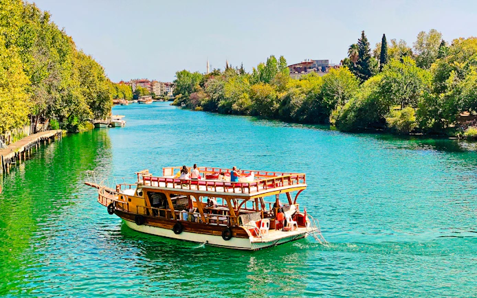 Cruise boat on Manavgat River with lush greenery, part of Dolphin Island tour.