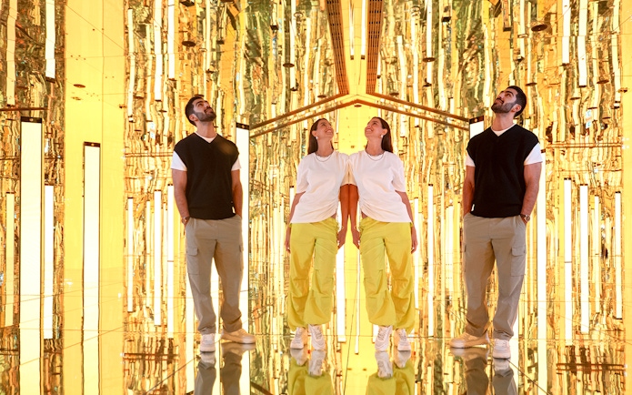 Couple exploring Tide installation at AYA Universe, surrounded by golden reflections.