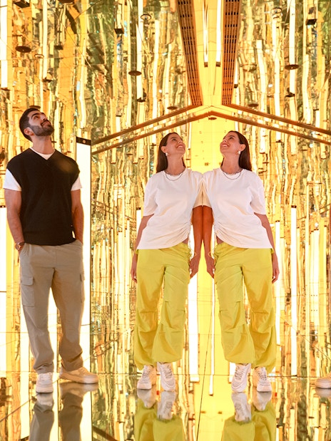 Couple exploring Tide installation at AYA Universe, surrounded by golden reflections.
