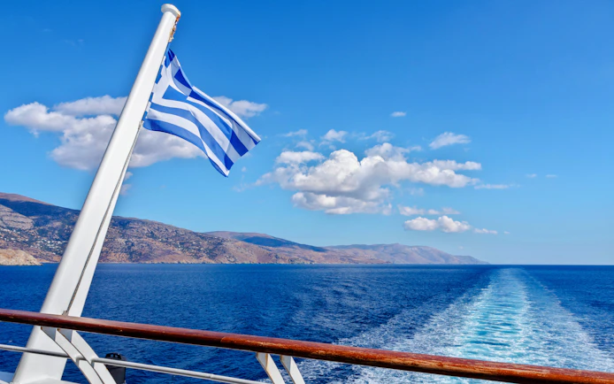 Greek flag on ferry with Tinos and Andros islands in Aegean Sea, Greece.