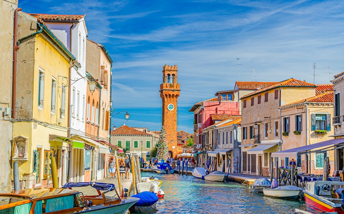 Murano island canal with boats and clock tower in the background, Venice, Italy.