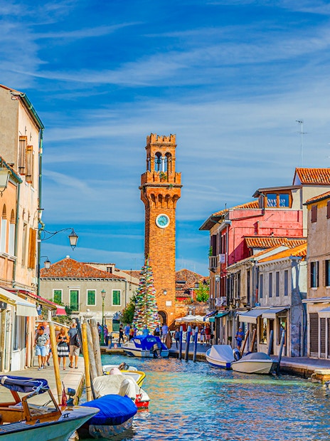 Murano island canal with boats and clock tower in the background, Venice, Italy.
