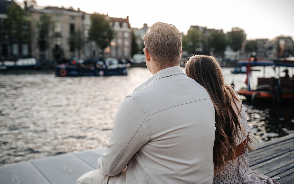 Couple sitting by the water near Magere Brug in Amsterdam during a professional photoshoot.