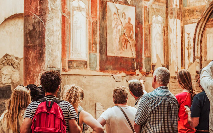 Tour group observing ancient frescoes at Herculaneum with expert guidance.