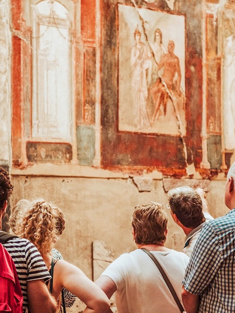 Tour group observing ancient frescoes at Herculaneum with expert guidance.