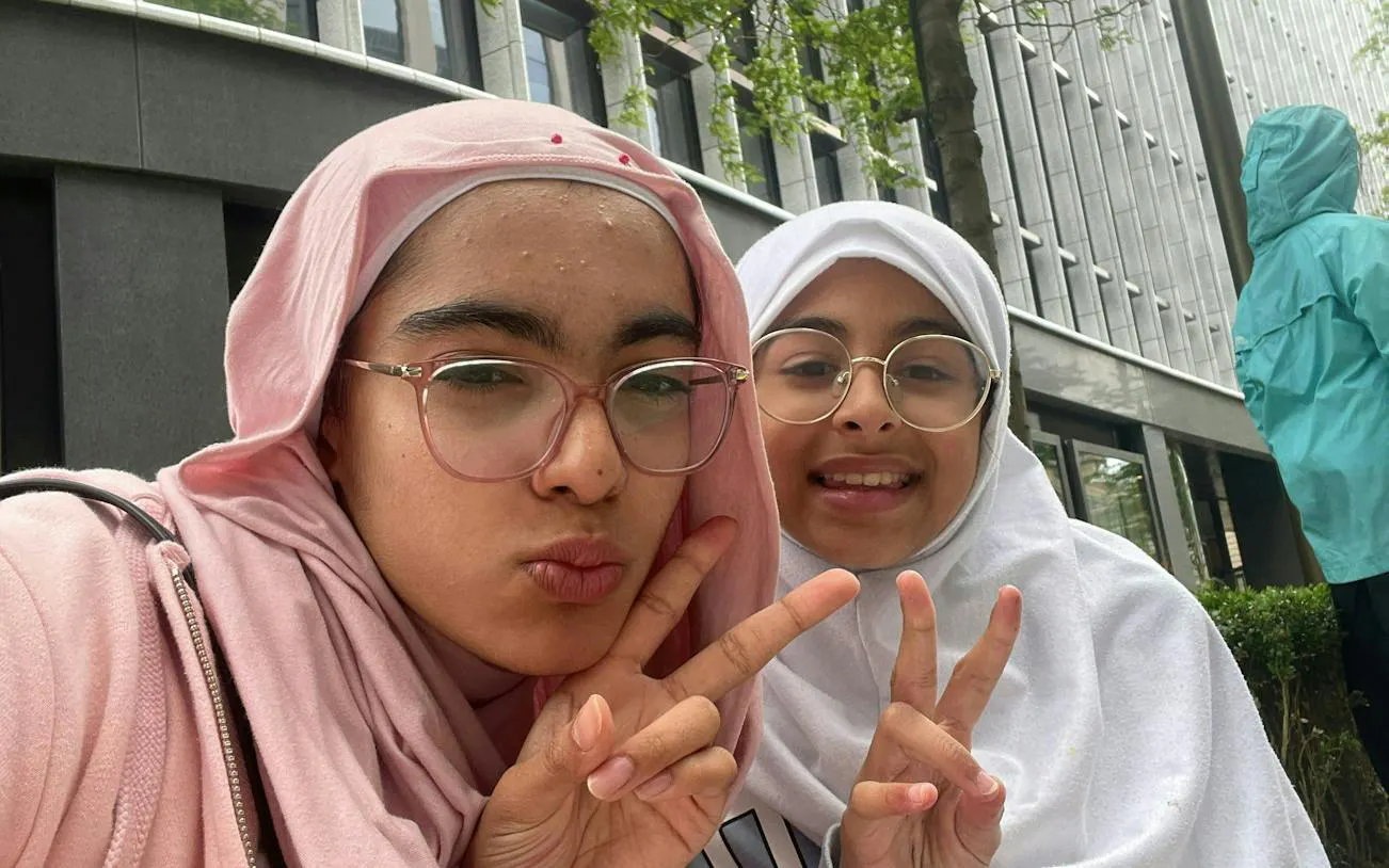Two people making peace signs in front of a modern building in Birmingham.