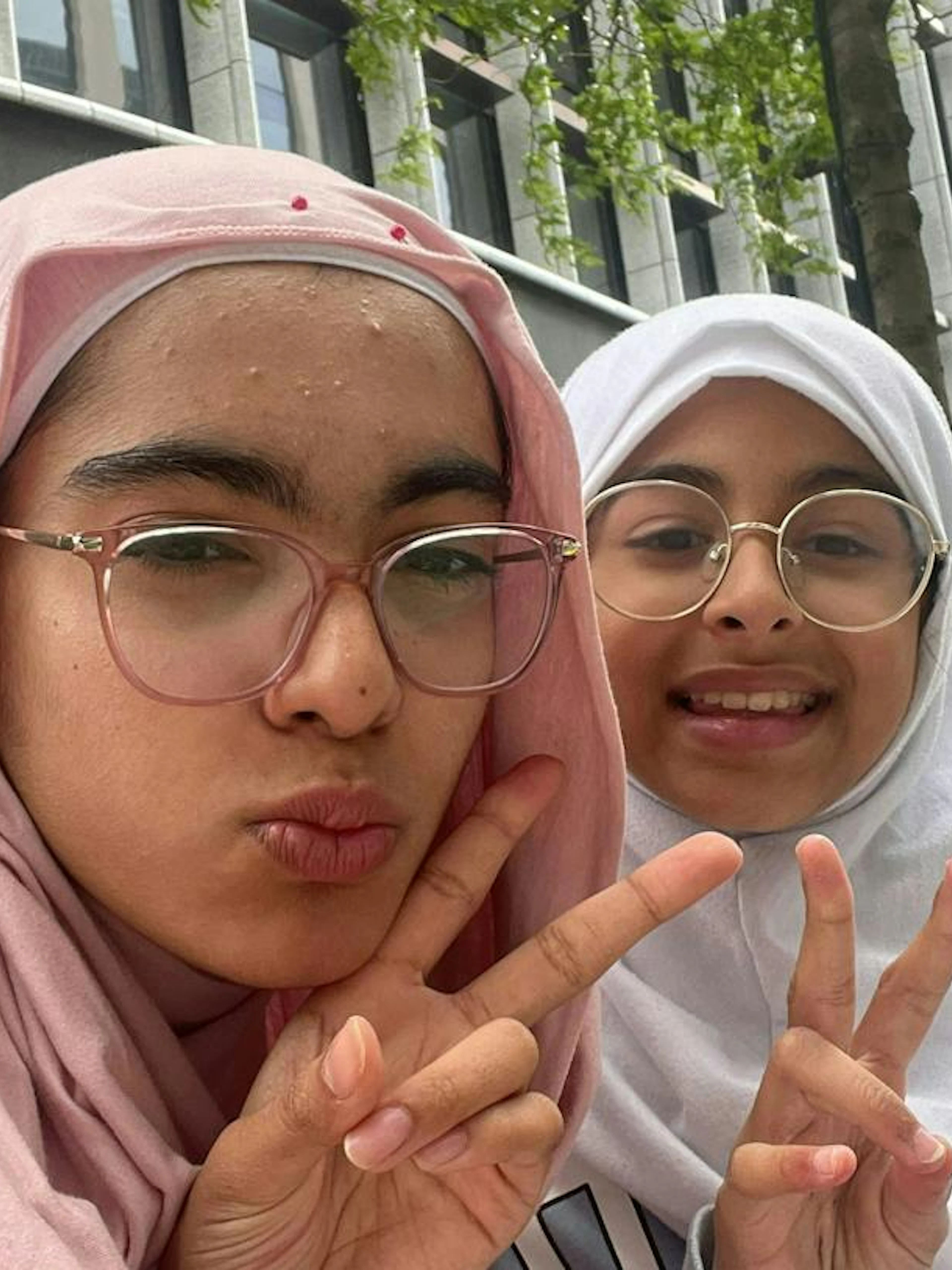 Two people making peace signs in front of a modern building in Birmingham.