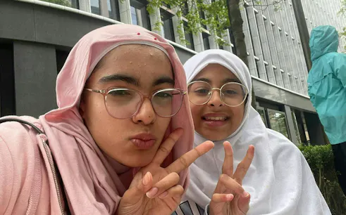 Two people making peace signs in front of a modern building in Birmingham.