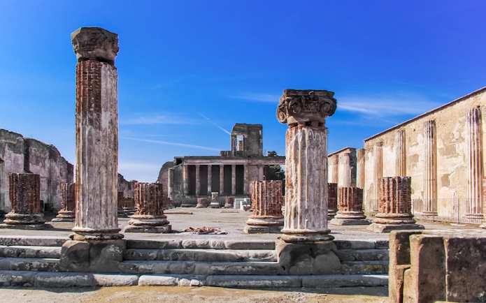 Ancient ruins of Pompeii with columns and temple remains under a clear blue sky.