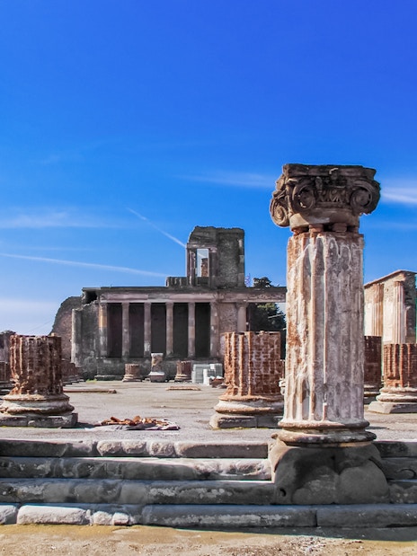 Ancient ruins of Pompeii with columns and temple remains under a clear blue sky.