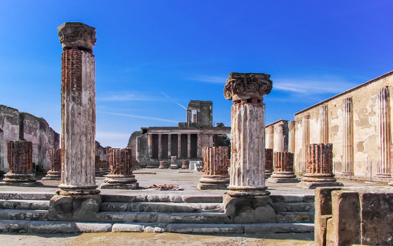 Ancient ruins of Pompeii with columns and temple remains under a clear blue sky.